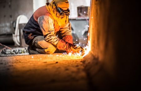 A demolition construction worker with full protective gear using a flame torch to cut up heavy machinery