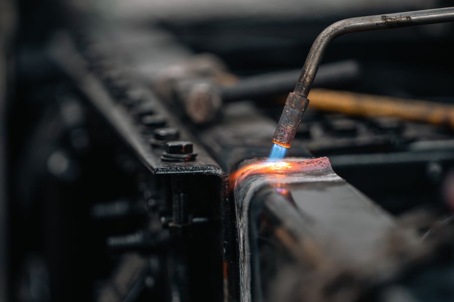 Close-up view of a welding torch heating a metal surface with a blue flame