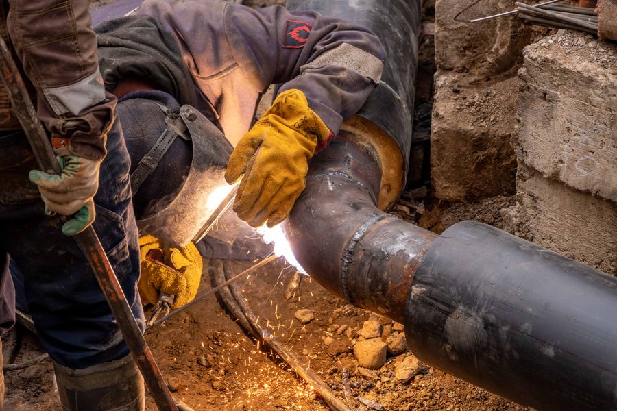 Welder in protective gear joining steel pipe sections in an industrial setting